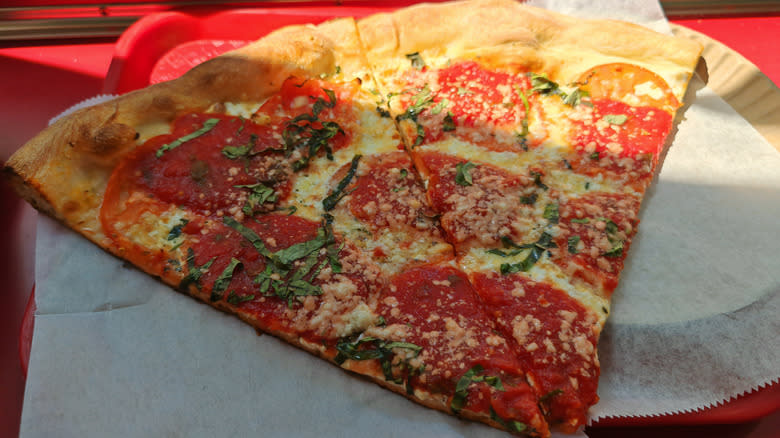 Tanka pizza s feferonima u NYC stilu s nasjeckanim bosiljkom i sirom na papirnatom tanjuru i crvenom pladnju