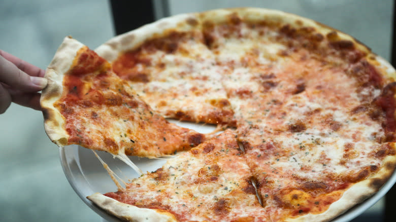Osoba izvuče komad cijele pizze u stilu New Yorka